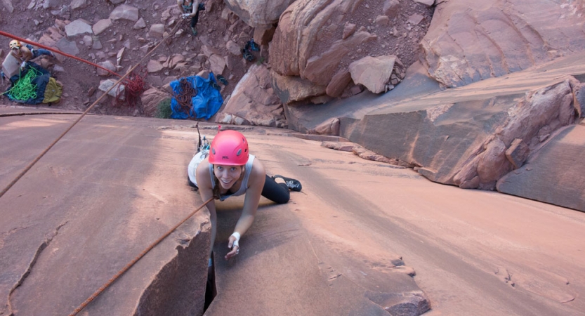 a student smiles at the camera as they climb a crag